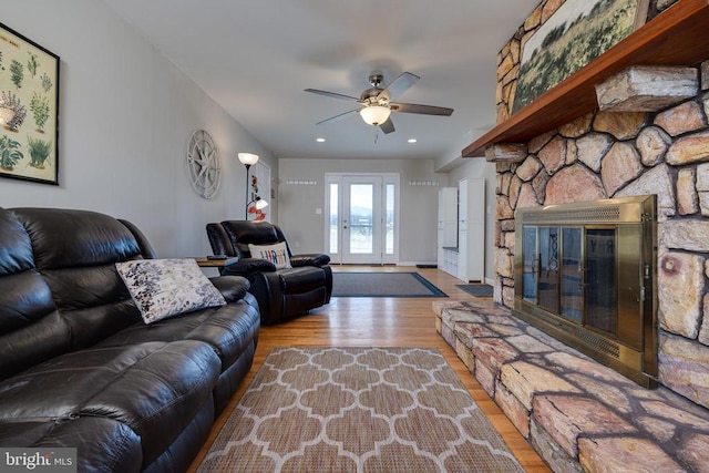living area with wood finished floors, a stone fireplace, ceiling fan, and recessed lighting