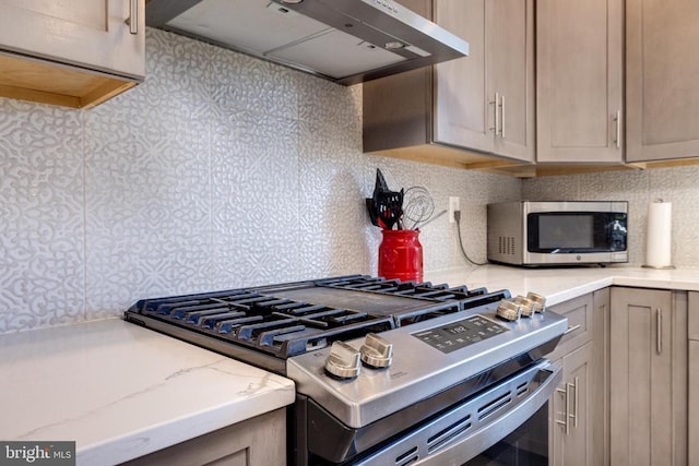 kitchen featuring under cabinet range hood, appliances with stainless steel finishes, tasteful backsplash, light stone counters, and gray cabinets