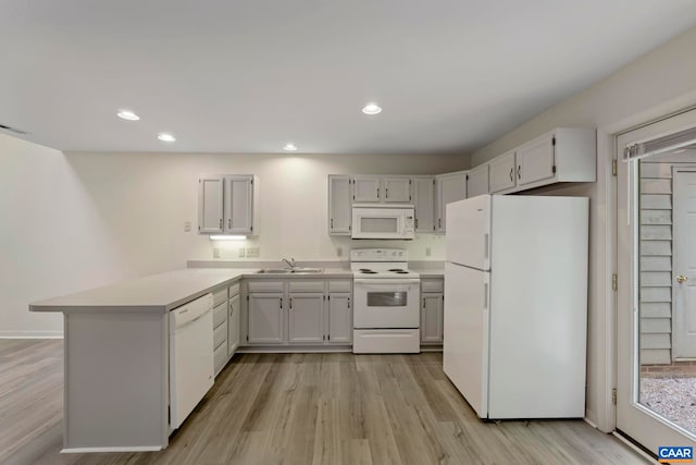 kitchen featuring a sink, a peninsula, white appliances, light wood finished floors, and light countertops