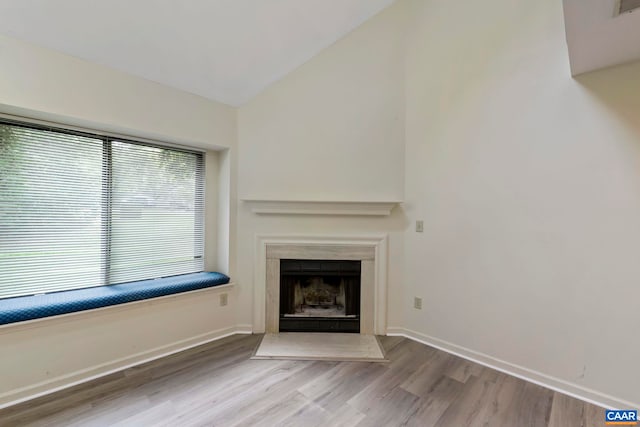unfurnished living room featuring vaulted ceiling, baseboards, a fireplace with flush hearth, and wood finished floors