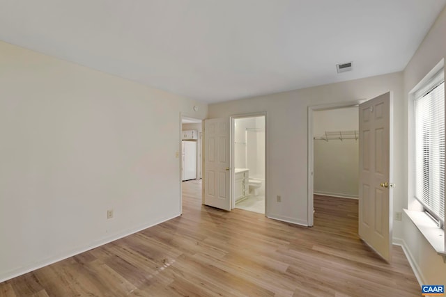 unfurnished bedroom featuring light wood finished floors, a walk in closet, baseboards, and visible vents