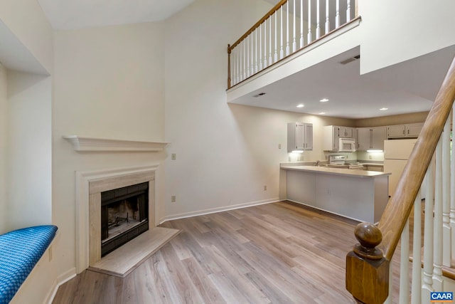 living area with light wood-style flooring, a fireplace with raised hearth, baseboards, and visible vents