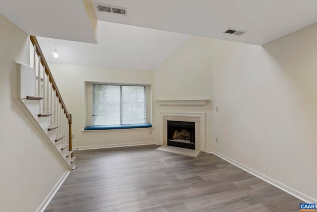unfurnished living room with lofted ceiling, a fireplace with flush hearth, visible vents, and wood finished floors