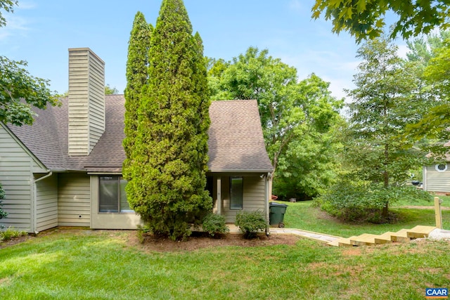exterior space featuring a shingled roof, a chimney, and a lawn
