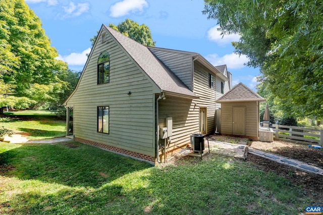 view of side of property featuring a yard, fence, a shed, central AC, and a shingled roof