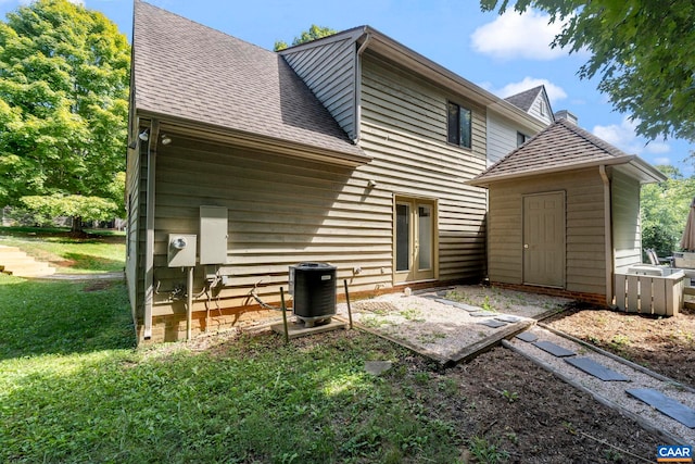back of property with a storage unit, a yard, an outbuilding, cooling unit, and a shingled roof