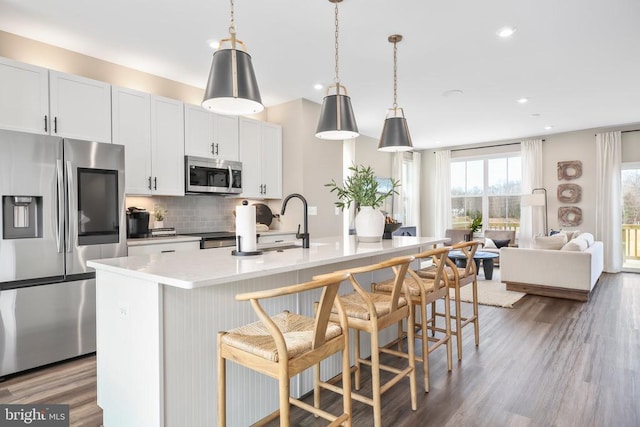 7713 Harlow Cir, Spotsylvania, VA 22551 - kitchen featuring appliances with stainless steel finishes, backsplash, wood finished floors, an island with sink, and a breakfast bar
