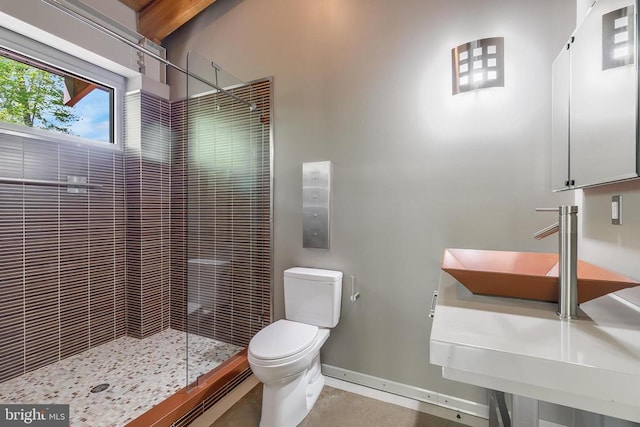 bathroom with toilet, a tile shower, and baseboards
