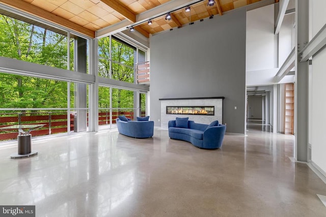 unfurnished living room featuring wood ceiling, a towering ceiling, finished concrete floors, a glass covered fireplace, and beam ceiling