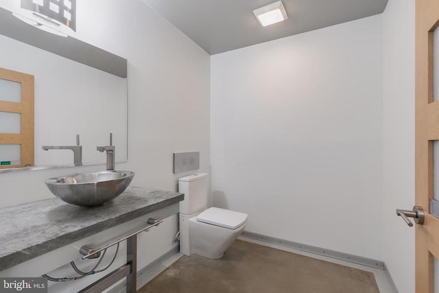 half bath featuring a sink, concrete flooring, toilet, and baseboards