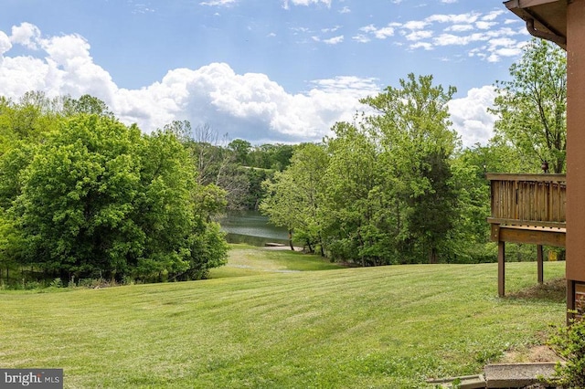 view of grassy yard featuring a deck with water view