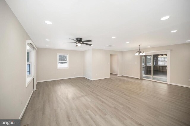 unfurnished living room with ceiling fan with notable chandelier and hardwood / wood-style floors