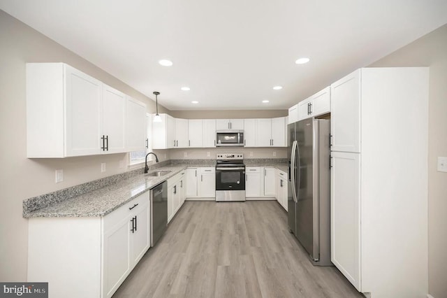 kitchen with sink, white cabinetry, hanging light fixtures, stainless steel appliances, and light stone countertops