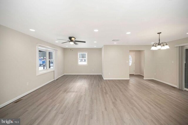 spare room with ceiling fan with notable chandelier and light wood-type flooring