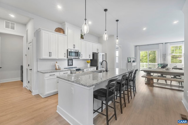 1802 Flora Ln, Charlottesville, VA 22911 - kitchen with stainless steel appliances, a center island with sink, white cabinets, light wood finished floors, and recessed lighting