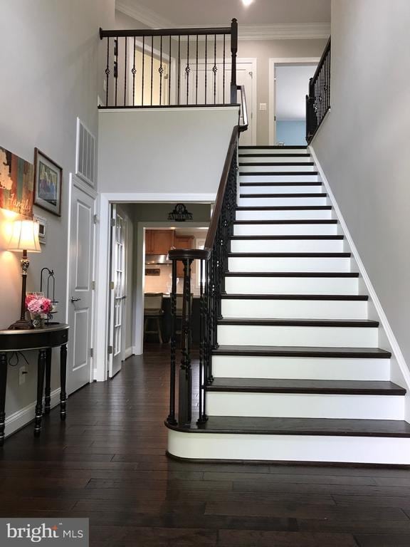  - staircase featuring wood finished floors, crown molding, visible vents, baseboards, and a towering ceiling