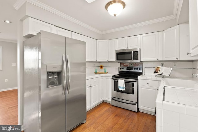 6314 Foster Rd, Spotsylvania, VA 22553 - kitchen featuring appliances with stainless steel finishes, tile countertops, ornamental molding, white cabinetry, and backsplash