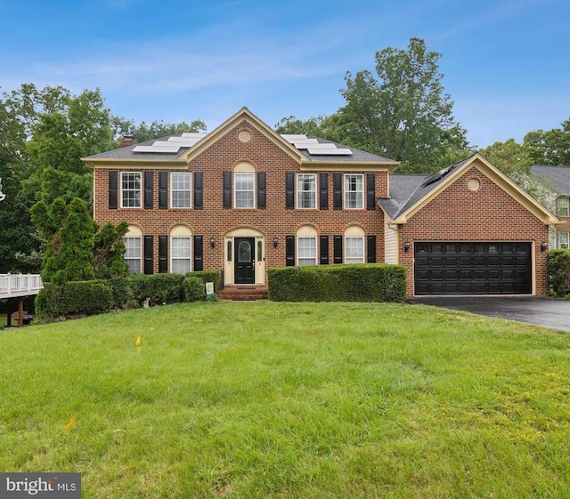 3803 Fallwood Ln, Fredericksburg, VA 22408 - colonial house featuring a front lawn, brick siding, driveway, a garage, and roof mounted solar panels