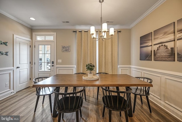 dining room featuring a chandelier, wood finished floors, ornamental molding, a decorative wall, and a wainscoted wall