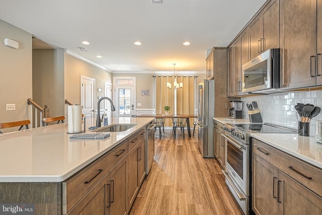 kitchen with appliances with stainless steel finishes, a sink, light wood finished floors, a chandelier, and crown molding