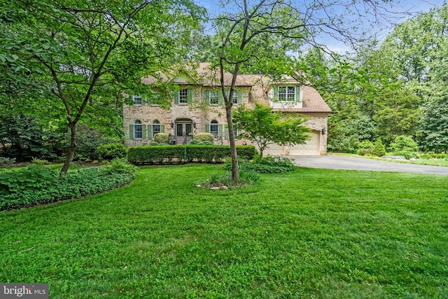 - view of front facade featuring asphalt driveway, brick siding, a front yard, and an attached garage