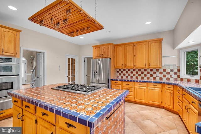  - kitchen featuring stainless steel appliances, a kitchen island, backsplash, tile counters, and a warming drawer