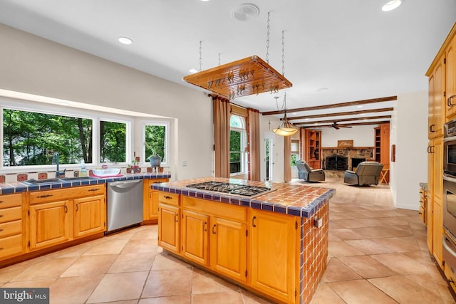  - kitchen featuring appliances with stainless steel finishes, tile counters, a fireplace, a kitchen island, and a ceiling fan
