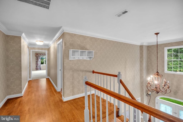  - hallway with wood finished floors, a chandelier, an upstairs landing, ornamental molding, and wallpapered walls
