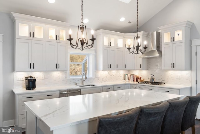  - kitchen with wall chimney range hood, a chandelier, appliances with stainless steel finishes, a center island, and decorative backsplash