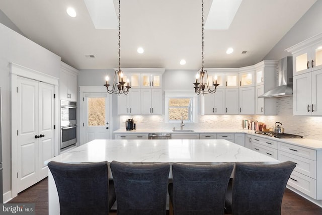  - kitchen featuring wall chimney range hood, a chandelier, a skylight, stainless steel appliances, and recessed lighting