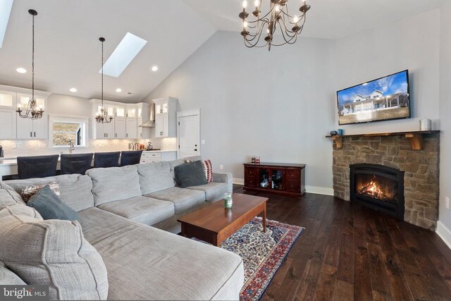  - living area featuring a chandelier, high vaulted ceiling, a stone fireplace, dark wood finished floors, and a skylight
