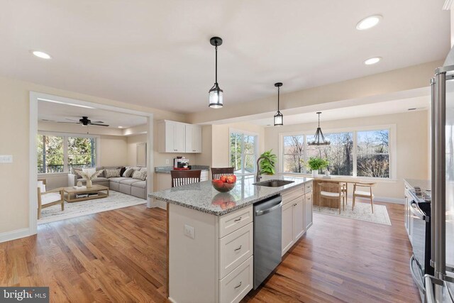 kitchen featuring an island with sink, white cabinets, hanging light fixtures, light stone counters, and stainless steel appliances