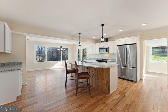 kitchen with pendant lighting, white cabinets, light stone counters, stainless steel appliances, and light hardwood / wood-style flooring