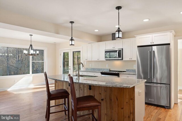 kitchen featuring sink, white cabinetry, stainless steel appliances, light stone counters, and a center island with sink