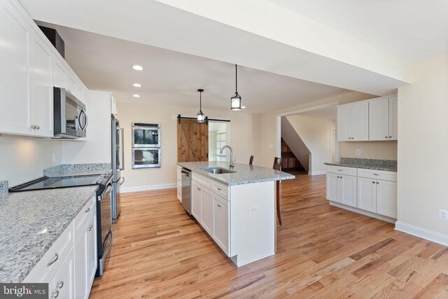 kitchen with sink, appliances with stainless steel finishes, white cabinets, decorative light fixtures, and a barn door