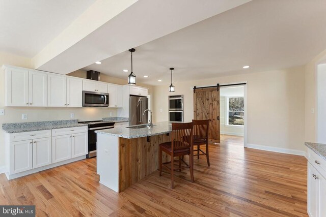 kitchen featuring stainless steel appliances, a barn door, a center island with sink, and white cabinets