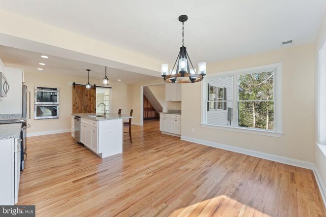 kitchen with pendant lighting, sink, white cabinetry, an island with sink, and a barn door