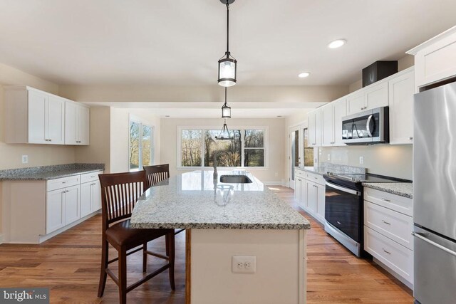 kitchen with appliances with stainless steel finishes, pendant lighting, an island with sink, sink, and white cabinets