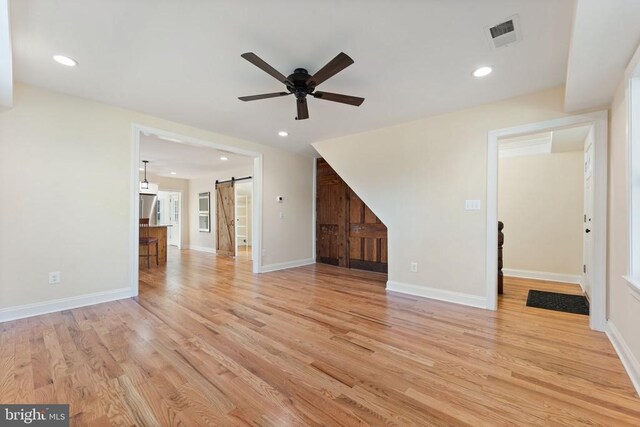 unfurnished living room featuring light hardwood / wood-style floors, a barn door, and ceiling fan