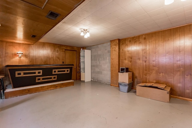 finished below grade area featuring wood walls, visible vents, and concrete block wall