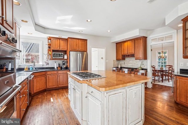 kitchen featuring appliances with stainless steel finishes, backsplash, open shelves, dark wood-style floors, and brown cabinets