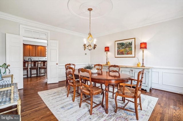 dining room with ornamental molding, dark wood-style flooring, wainscoting, a chandelier, and a decorative wall