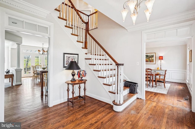 stairway with a chandelier, wood finished floors, ornamental molding, and ornate columns