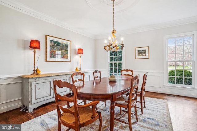 dining space with a chandelier, ornamental molding, a wainscoted wall, a decorative wall, and wood finished floors