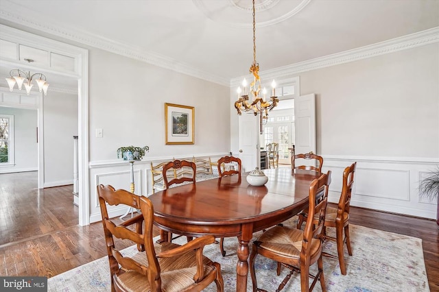 dining area featuring a chandelier, ornamental molding, wood finished floors, a wainscoted wall, and a decorative wall