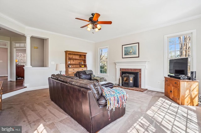 carpeted living area featuring ornamental molding, ceiling fan, decorative columns, baseboards, and a brick fireplace