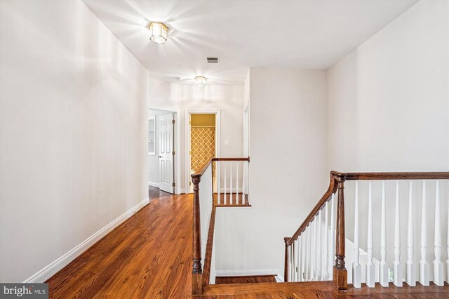 hallway with an upstairs landing, wood finished floors, and baseboards