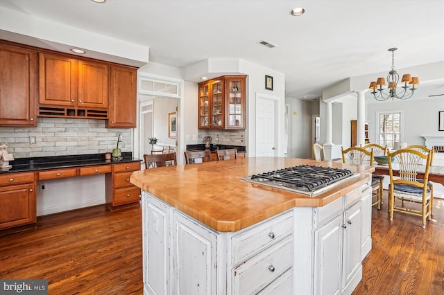 kitchen with stainless steel gas cooktop, dark wood finished floors, a chandelier, decorative backsplash, and glass insert cabinets