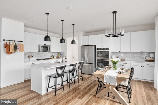 kitchen featuring stainless steel appliances, backsplash, a kitchen bar, an island with sink, and light countertops
