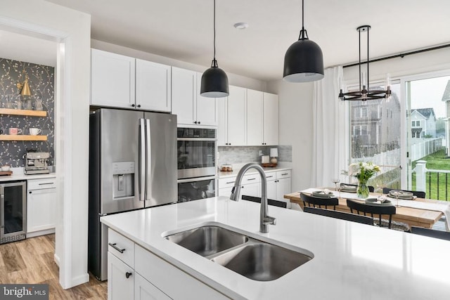 kitchen with stainless steel appliances, a sink, wine cooler, backsplash, and decorative light fixtures